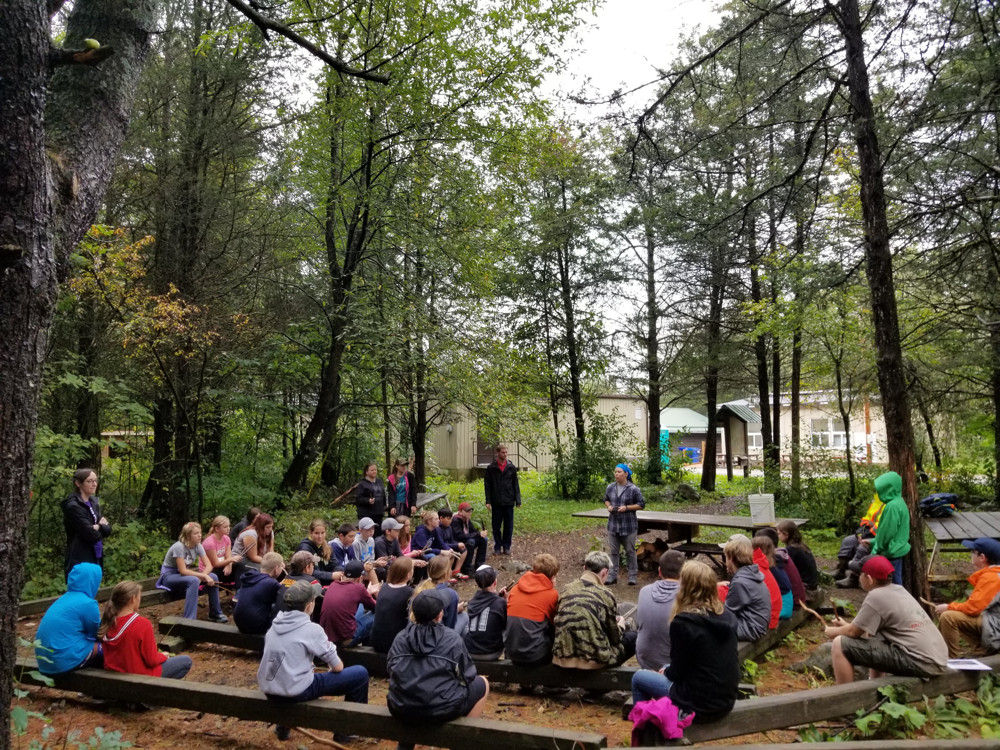 students sitting in a large circle in the forest with an instructor speaking to them