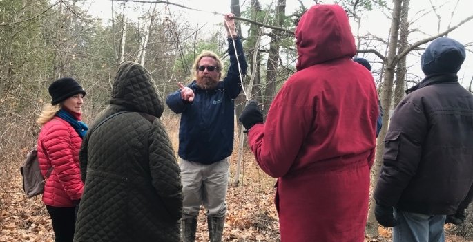 A man holds up a branch while talking to a small group of people.