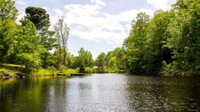 Scenic view of a serene lake surrounded by lush greenery under a partly cloudy sky.
