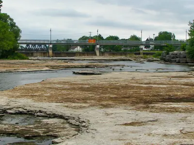 View of a shallow river with exposed rocky bed leading towards a bridge.