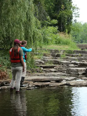 Two people stand by a rocky stream, pointing towards a dam.