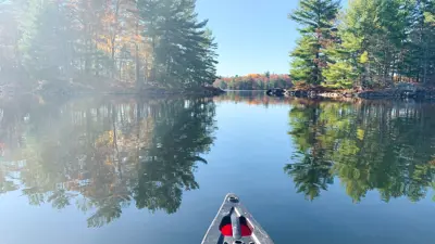 A serene view from a red canoe on a calm lake, with reflections of surrounding trees under a clear blue sky.