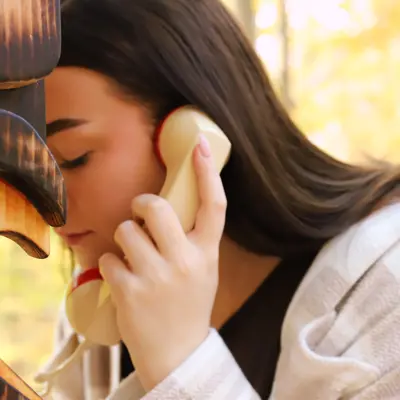 A woman in nature, stands at phone booth using a unconnected telephone 