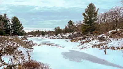 Snow-covered landscape with surrounding trees and rocky terrain under a cloudy sky.