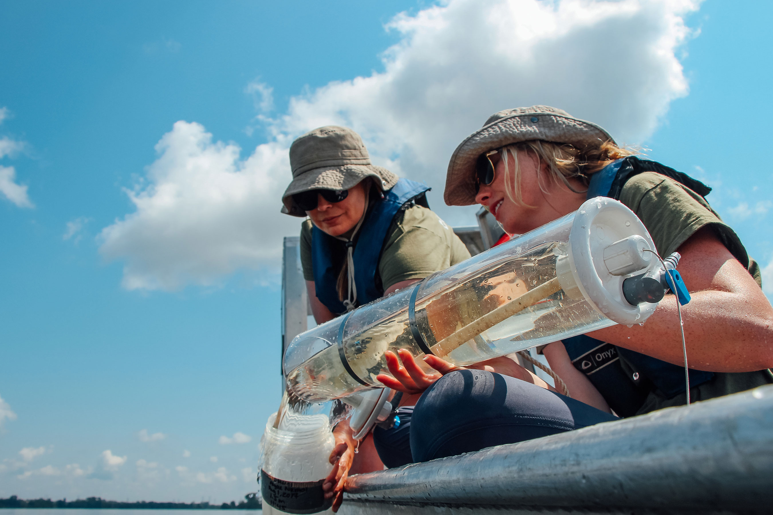 Two water monitors are examining water samples from a clear container onboard a boat.