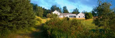 Path leading to a rural schoolhouse surrounded by lush greenery under a clear sky at dusk.